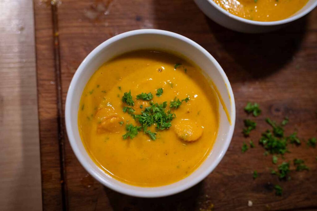 Fertige Kürbissuppe mit Kokosmilch, Curry, geschlagener Sahne und Kürbiskernöl im Teller angerichtet