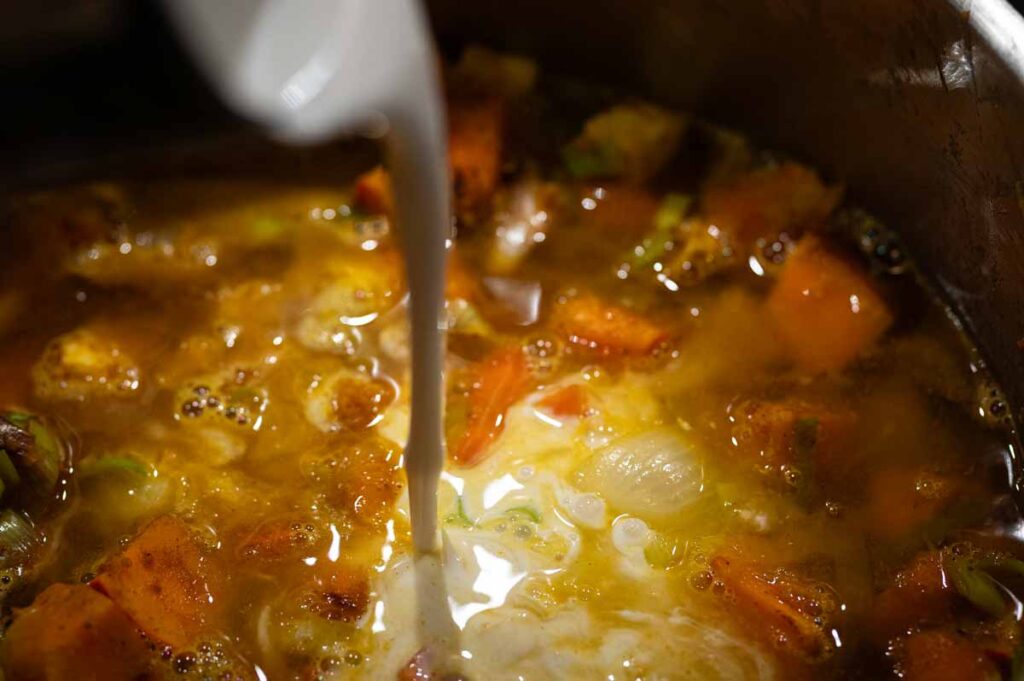 Kokosmilch und Currypulver werden in die pürierte Kürbissuppe eingerührt für eine cremige Konsistenz und würziges Aroma