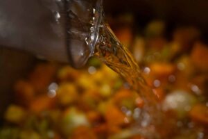 Angebratene Kürbisstücke werden mit Gemüsebrühe abgelöscht – Zubereitungsschritt für cremige Kürbissuppe