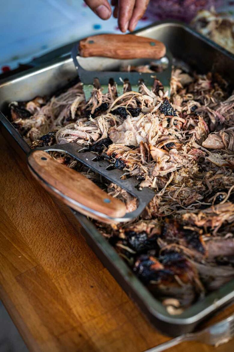 Zartes Pulled Pork aus dem Smoker, serviert auf einem Holzbrett mit BBQ-Soße und Burgerbrötchen.