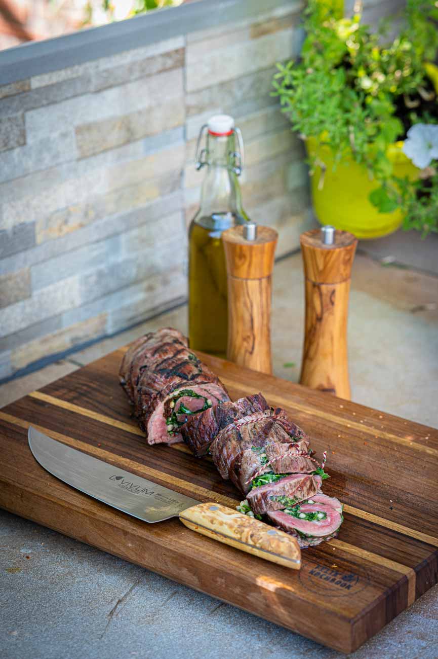 Saftige Flank Steak Rolle, gefüllt mit Rucola, Parmesan und Chimichurri, aufgeschnitten auf einem Holzbrett nach dem Grillen.