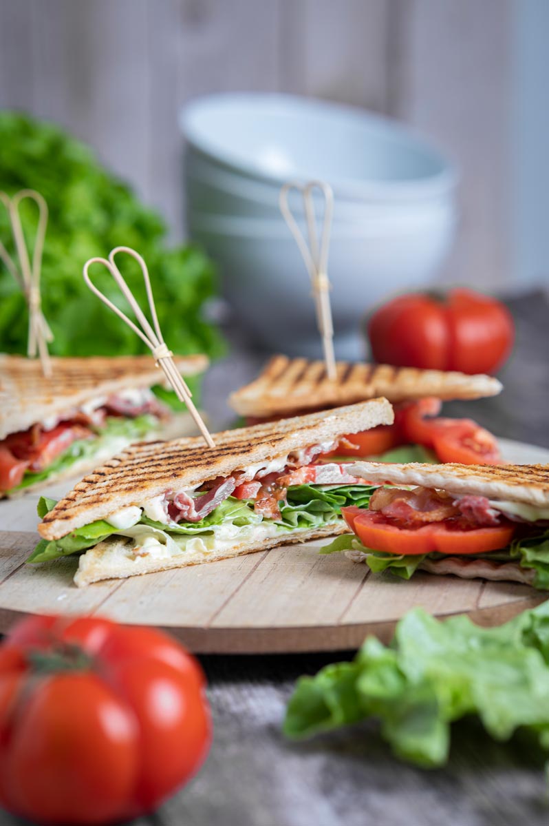 Frisch zubereitetes BLT Sandwich mit knusprigem Bacon, Tomatenscheiben, grünem Salat und geröstetem Toastbrot auf einem Holzbrett serviert.