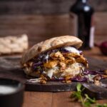 Nahaufnahme eines veganen Döners mit knusprigem Räuchertofu, Rotkohl, Zwiebelsalat und Tzaziki in warmem Fladenbrot.