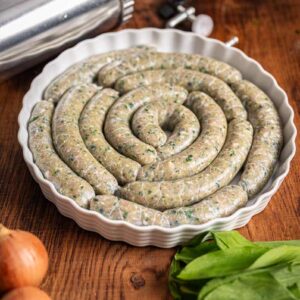Roh gefüllte Bärlauch Bratwürste auf einem Holzbrett, umgeben von frischem Bärlauch und Gewürzen, bereit für den Grill oder die Pfanne.
