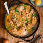 Coq au Vin Blanc in einer Pfanne mit cremiger Weißweinsoße, Champignons und frischer Petersilie.