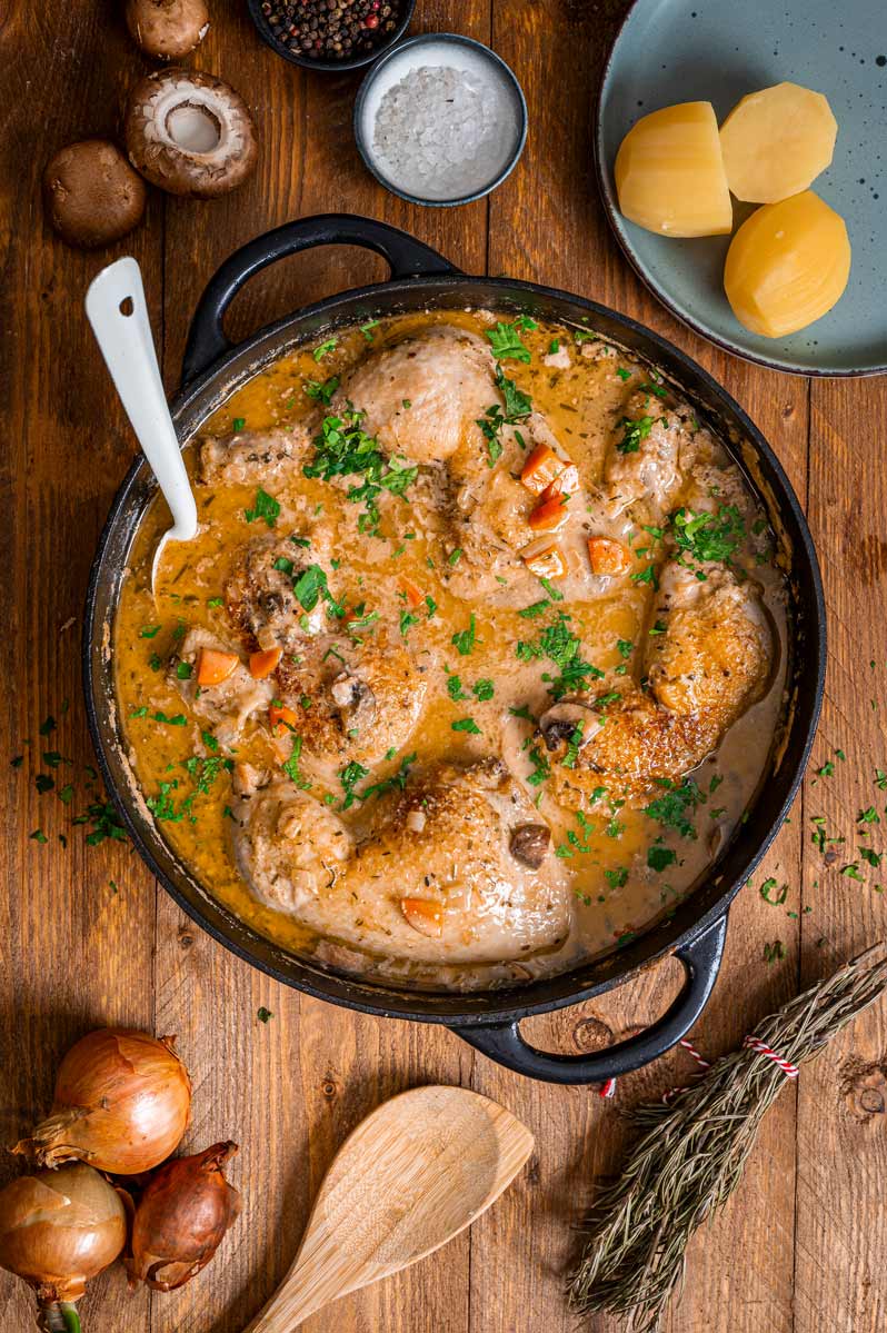 Coq au Vin Blanc in einer Pfanne mit cremiger Weißweinsoße, Champignons und frischer Petersilie.