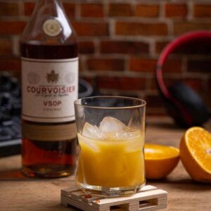 Ein erfrischender Sunshine Cocktail aus 90 ml Cognac, 60 ml Orangensaft und 30 ml Zuckersirup, garniert mit einer Maraschino Kirsche und Orangenzeste, serviert auf Eis.