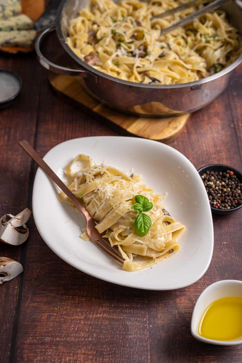 Tagliatelle werden in Gorgonzola Käsesoße geschwenkt und mit Trüffelöl verfeinert, bevor sie auf einem Teller angerichtet werden.