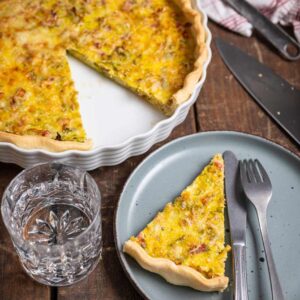 Goldbraun gebackene Lauch Quiche mit Speck und Gouda auf einem rustikalen Holztisch, serviert in einer runden Tarteform.