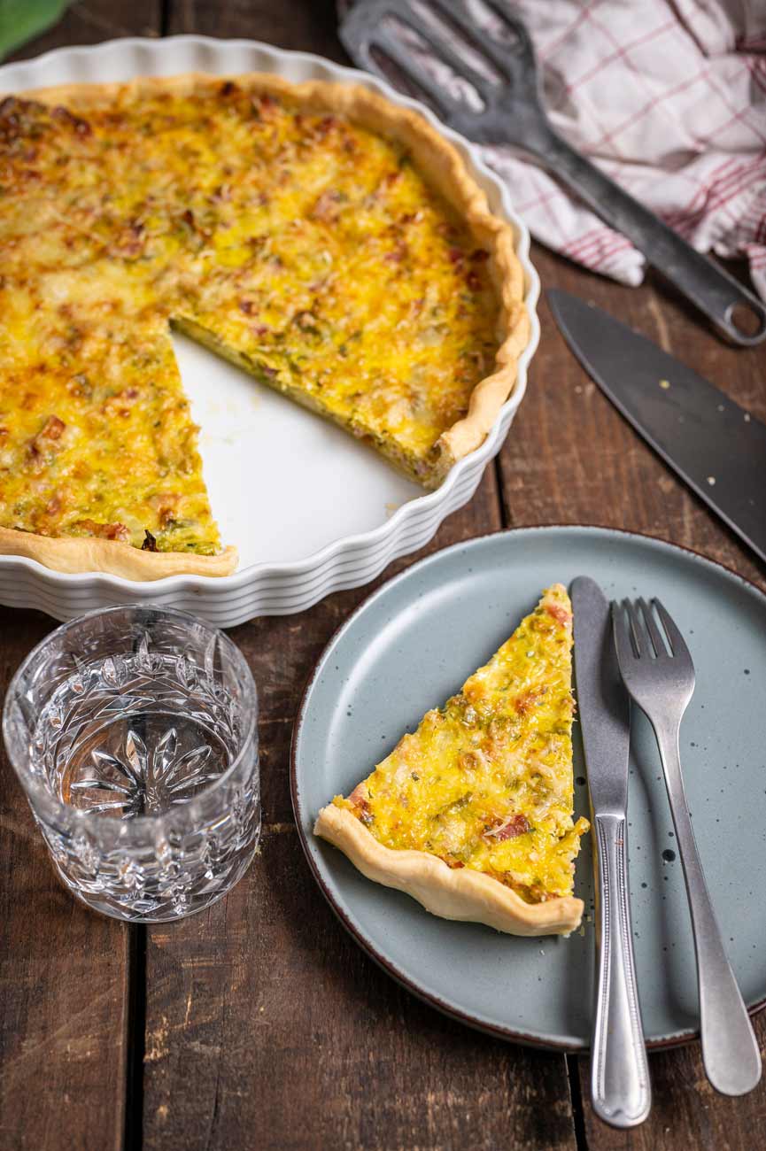 Goldbraun gebackene Lauch Quiche mit Speck und Gouda auf einem rustikalen Holztisch, serviert in einer runden Tarteform.
