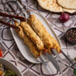 Servierter Hähnchen Koobideh Kebab auf einem Teller mit Reis, Sumach und Butter