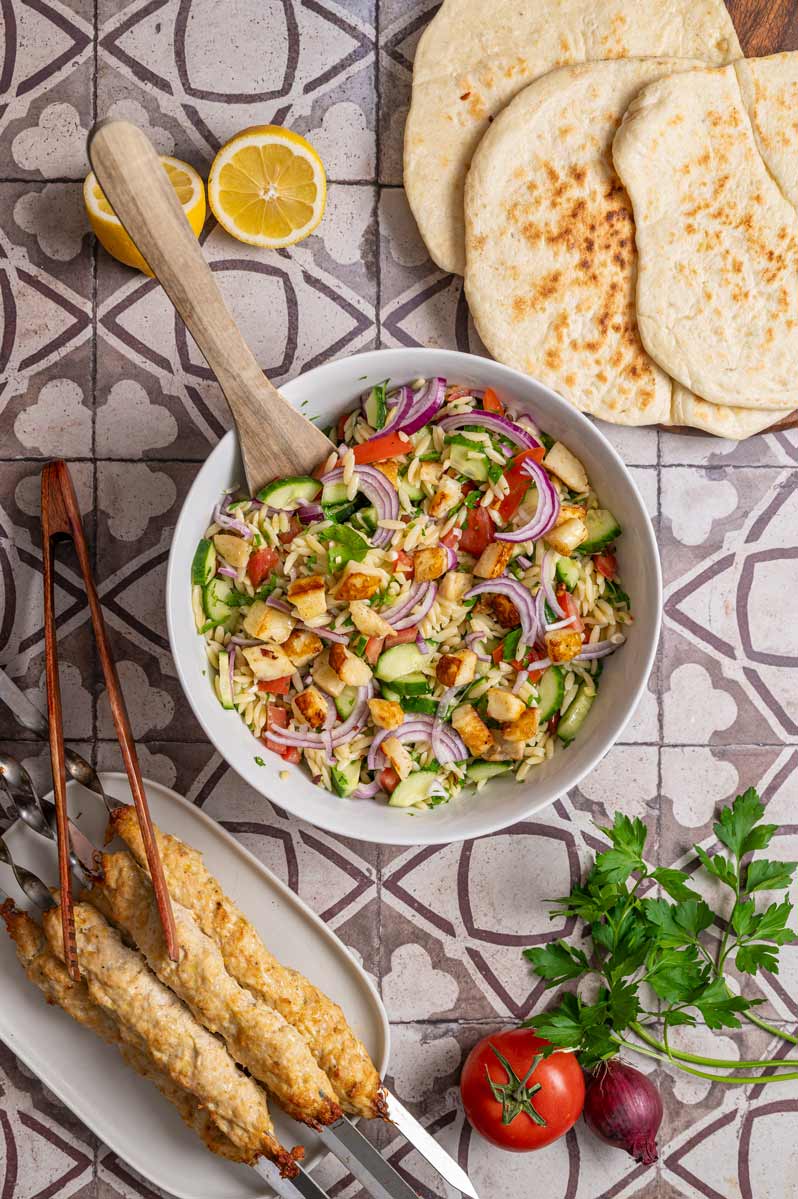 Angerichteter Kritharaki Salat mit gebratenem Halloumi, Gurke, Paprika und Zwiebeln in einer Schüssel