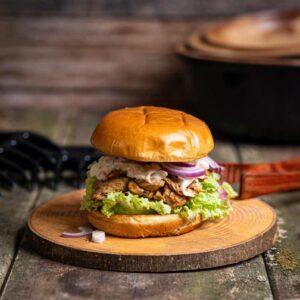 Frisch zubereiteter Pulled Chicken Burger mit saftigem Hähnchenfleisch, Cole Slaw, roten Zwiebelringen und grünem Salat im gerösteten Burger Bun