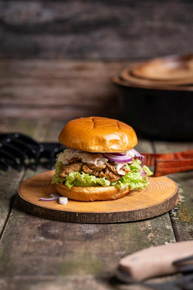 Frisch zubereiteter Pulled Chicken Burger mit saftigem Hähnchenfleisch, Cole Slaw, roten Zwiebelringen und grünem Salat im gerösteten Burger Bun