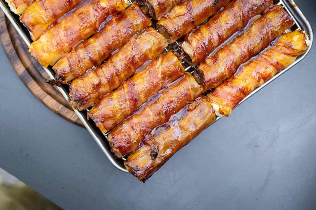 Fertige Shotgun Shells vom Grill mit knusprigem Bacon und Hackfleischfüllung auf einem Holzbrett serviert
