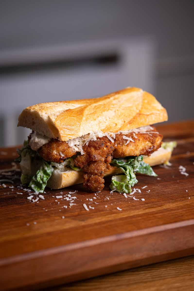 Frisch frittiertes Hähnchenfilet wird in Sandwich mit Caesar Dressing und Salat gelegt