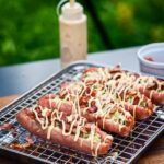 Detailaufnahme vom Bacon-Topping auf der Cheeseburger Bratwurst mit cremiger Burger Soße und geschmolzenem Käse