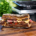 Überlaufende Chili Cheese Sauce auf einem herzhaften Steak Sandwich mit Paprika und Zwiebeln