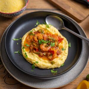 Cremige Grits mit saftigen Garnelen und knusprigem Bacon auf einem weißen Teller, garniert mit Frühlingszwiebeln