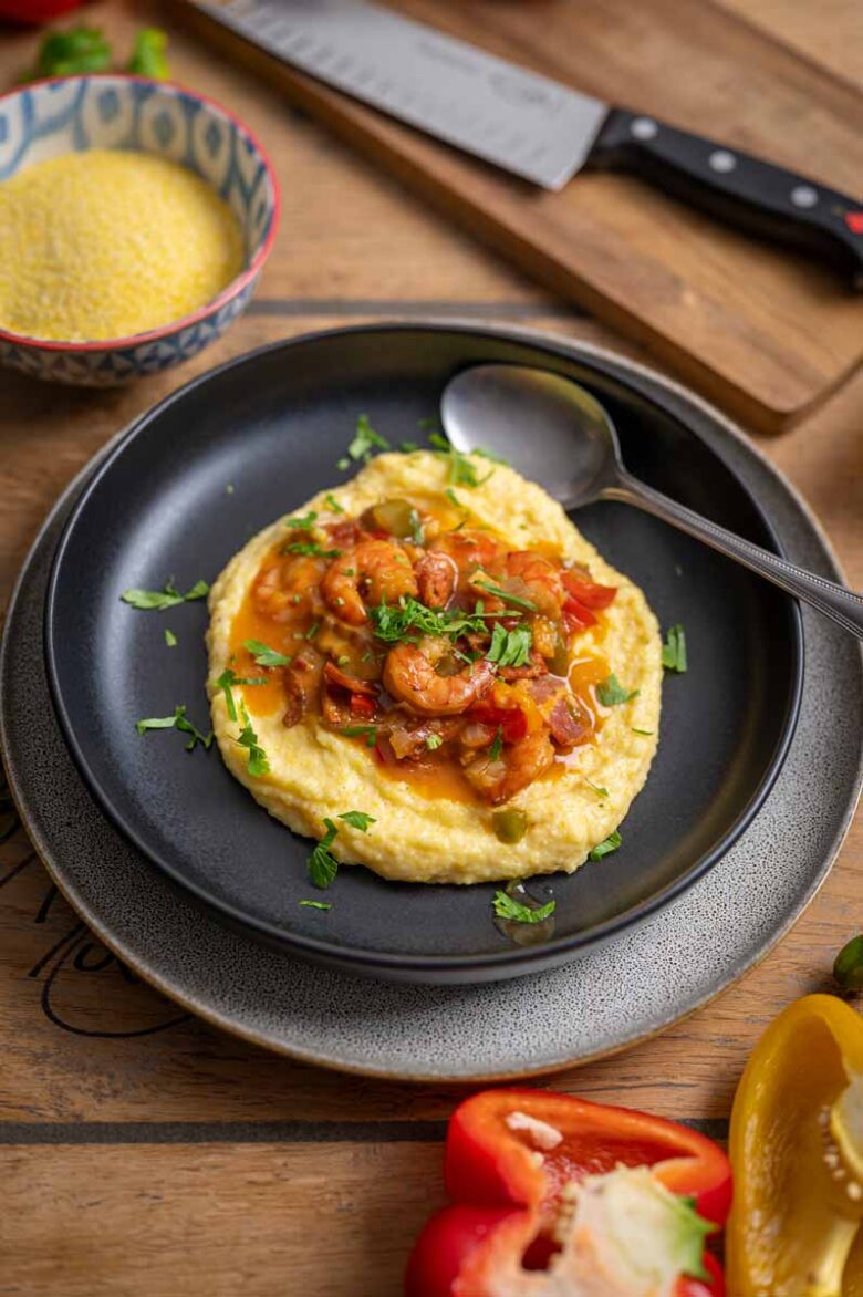 Cremige Grits mit saftigen Garnelen und knusprigem Bacon auf einem weißen Teller, garniert mit Frühlingszwiebeln