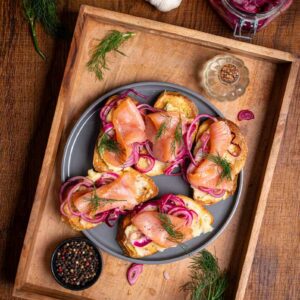 Nahaufnahme von gerösteten Brotscheiben mit Räucherlachs, Kartoffel-Knoblauch-Creme und rosa eingelegten Zwiebeln