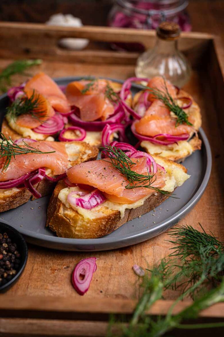 Detailansicht von Crostini mit Lachs, Skordalia, eingelegten Zwiebeln und frischem Dill als Topping