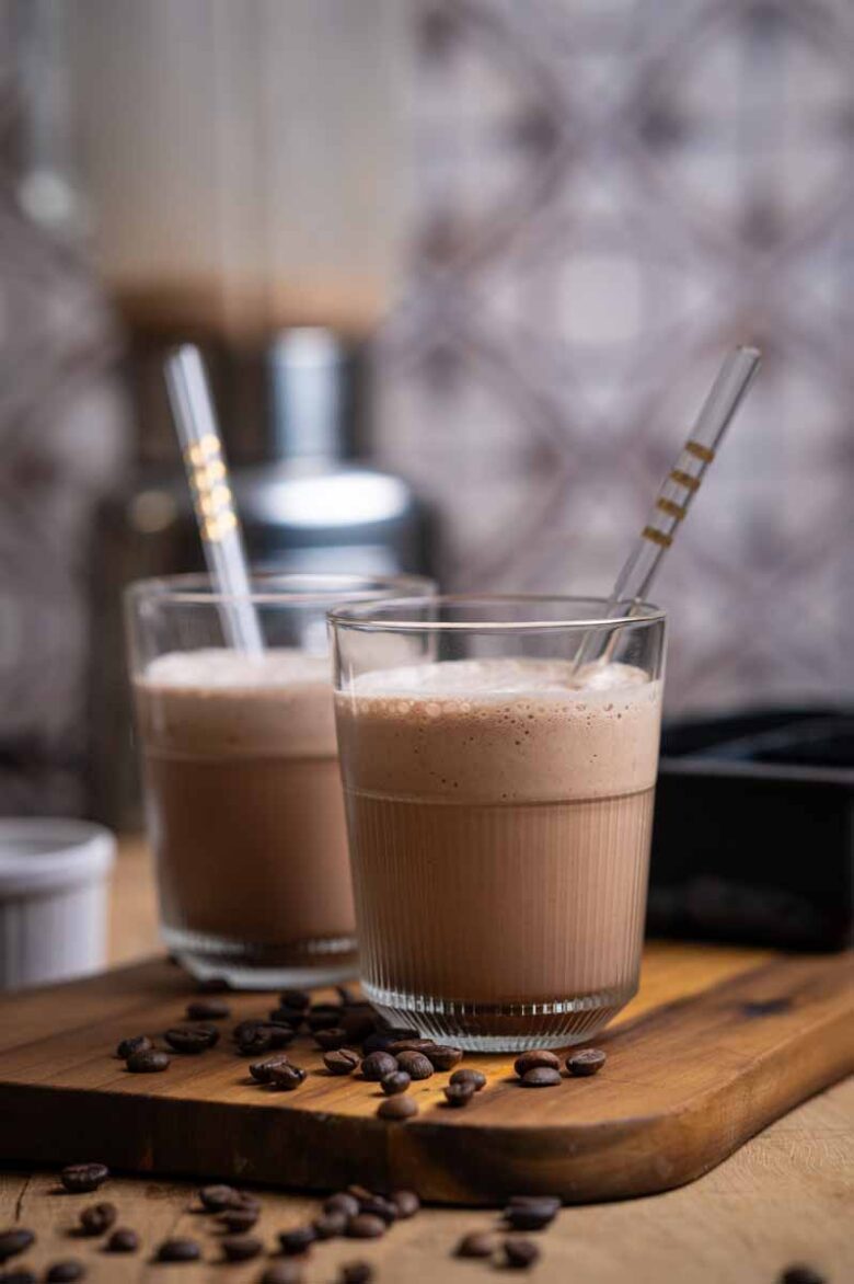 Cremiger Eiskaffee mit Kaffeeeiswürfeln, kalter Milch und Kakao – serviert im Glas mit Strohhalm