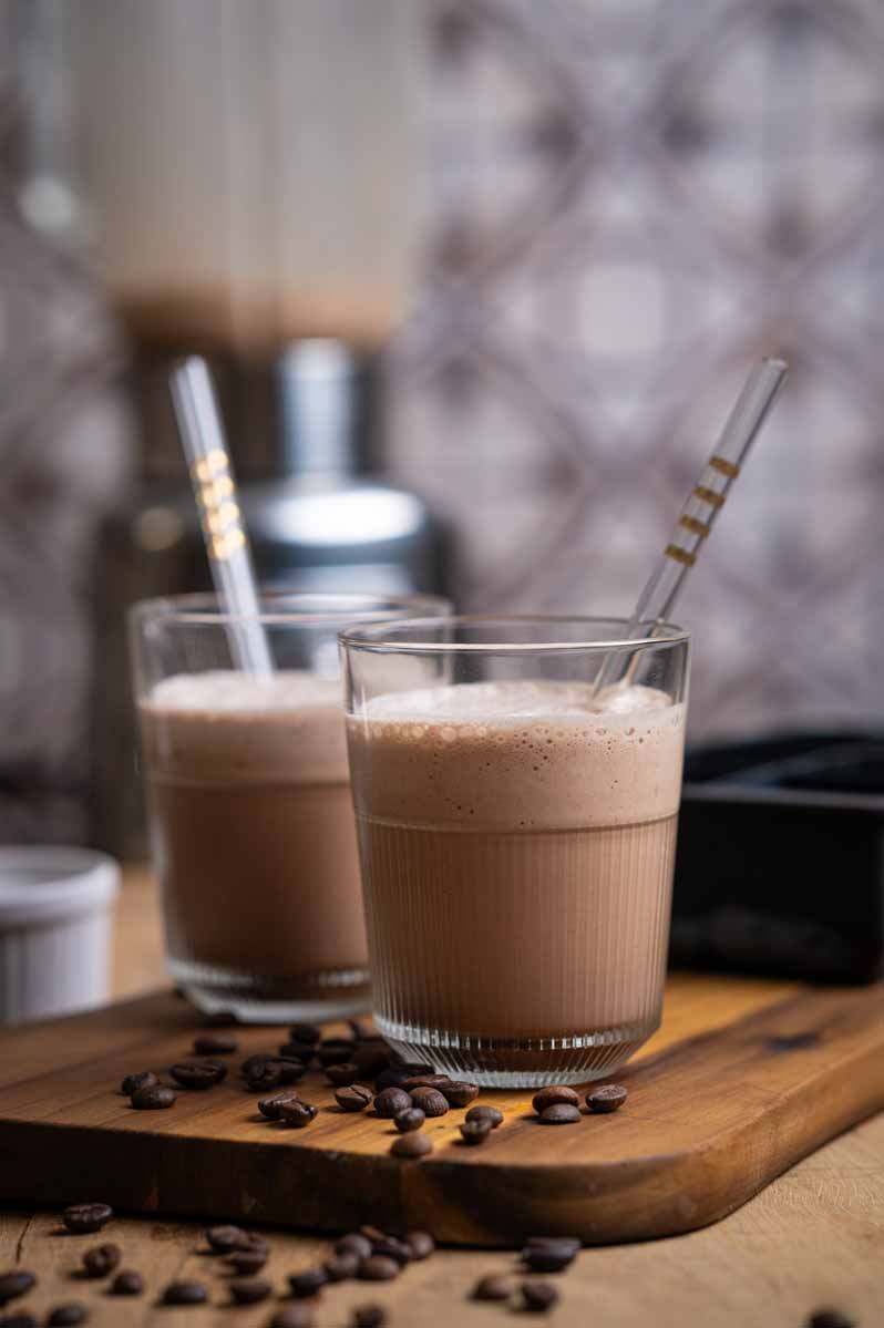 Cremiger Eiskaffee mit Kaffeeeiswürfeln, kalter Milch und Kakao – serviert im Glas mit Strohhalm