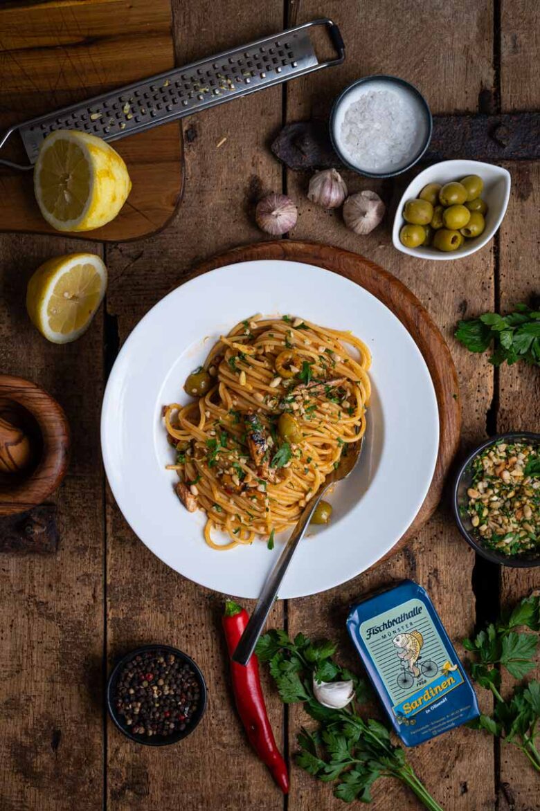 Sizilianische Pasta mit Sardinen, Oliven, Zitronensaft und gerösteten Pinienkernen auf einem Teller angerichtet