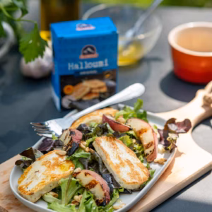 Bunter Sommersalat mit gegrillten Pfirsichen, Halloumi, Pinienkernen und frischem Grün auf einem Teller serviert.
