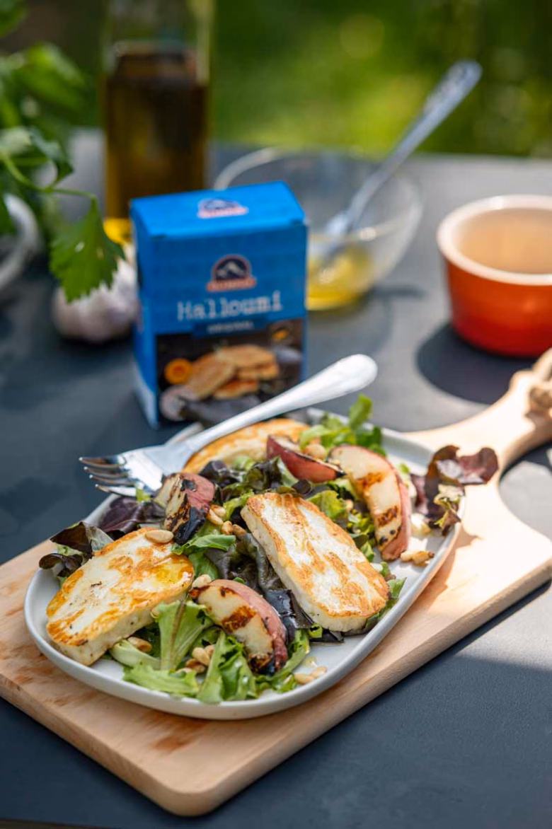 Bunter Sommersalat mit gegrillten Pfirsichen, Halloumi, Pinienkernen und frischem Grün auf einem Teller serviert.
