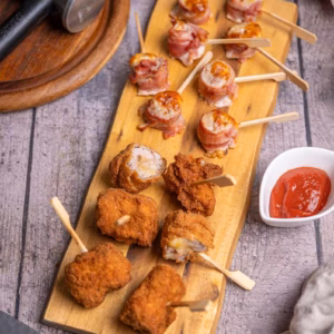 Zwei Varianten von Cordon Bleu Spießen auf einem Holzbrett, einmal mit knusprigem Bacon, einmal paniert und frittiert