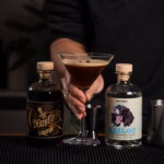 Fertiger Espresso Martini mit cremiger Schaumkrone und drei Kaffeebohnen als Garnitur im Martiniglas.