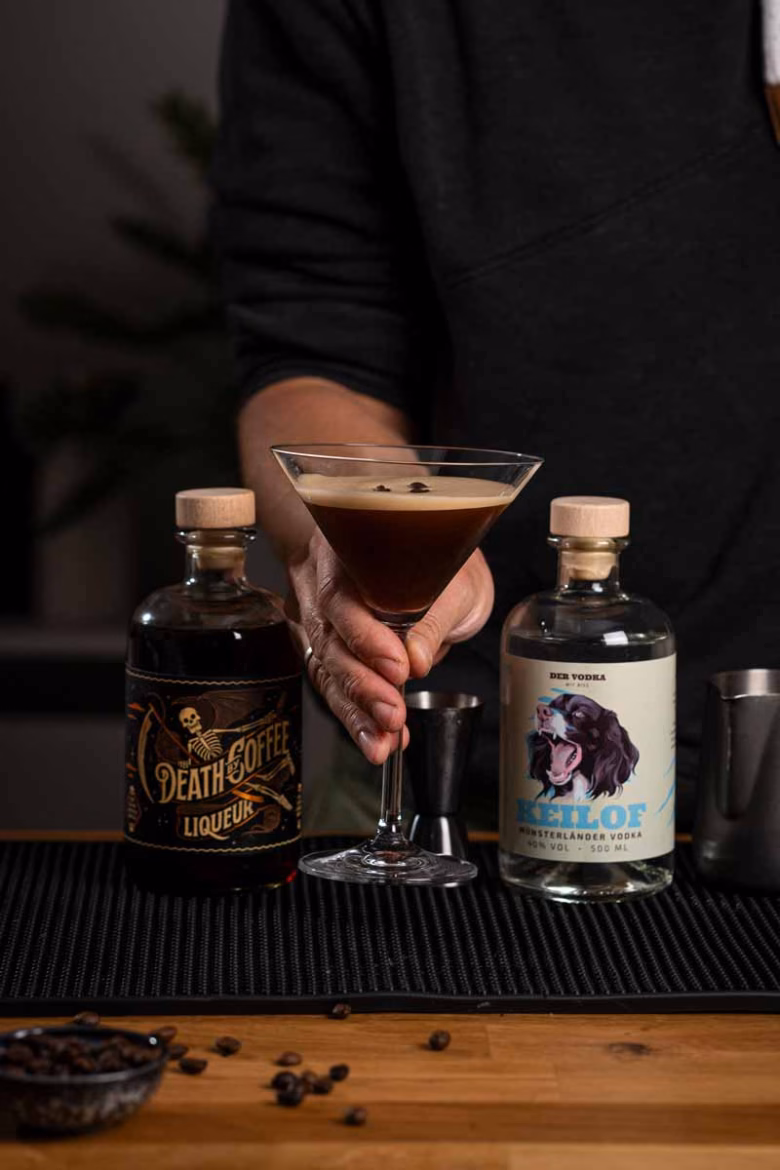Fertiger Espresso Martini mit cremiger Schaumkrone und drei Kaffeebohnen als Garnitur im Martiniglas.