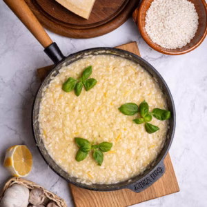 Risotto mit Zitrone in einer Pfanne, cremig gerührt und mit Basilikum verfeinert.