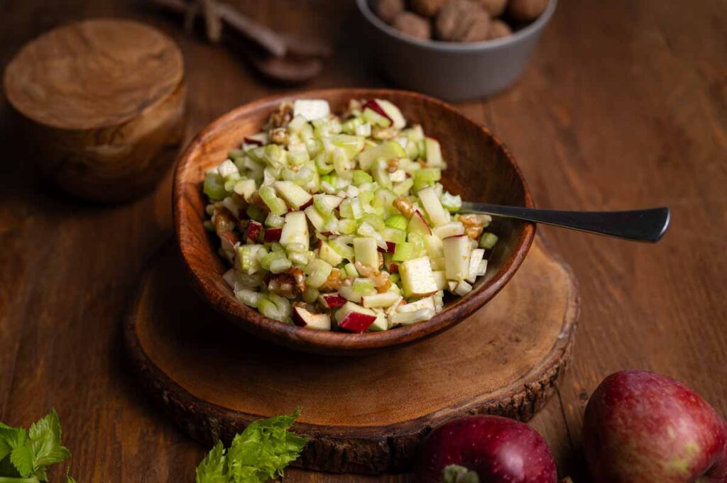 Frisch zubereiteter Sellerie Salat mit Apfel, Zitronensaft und Walnüssen, dekorativ mit Selleriestangen und Äpfeln im Hintergrund