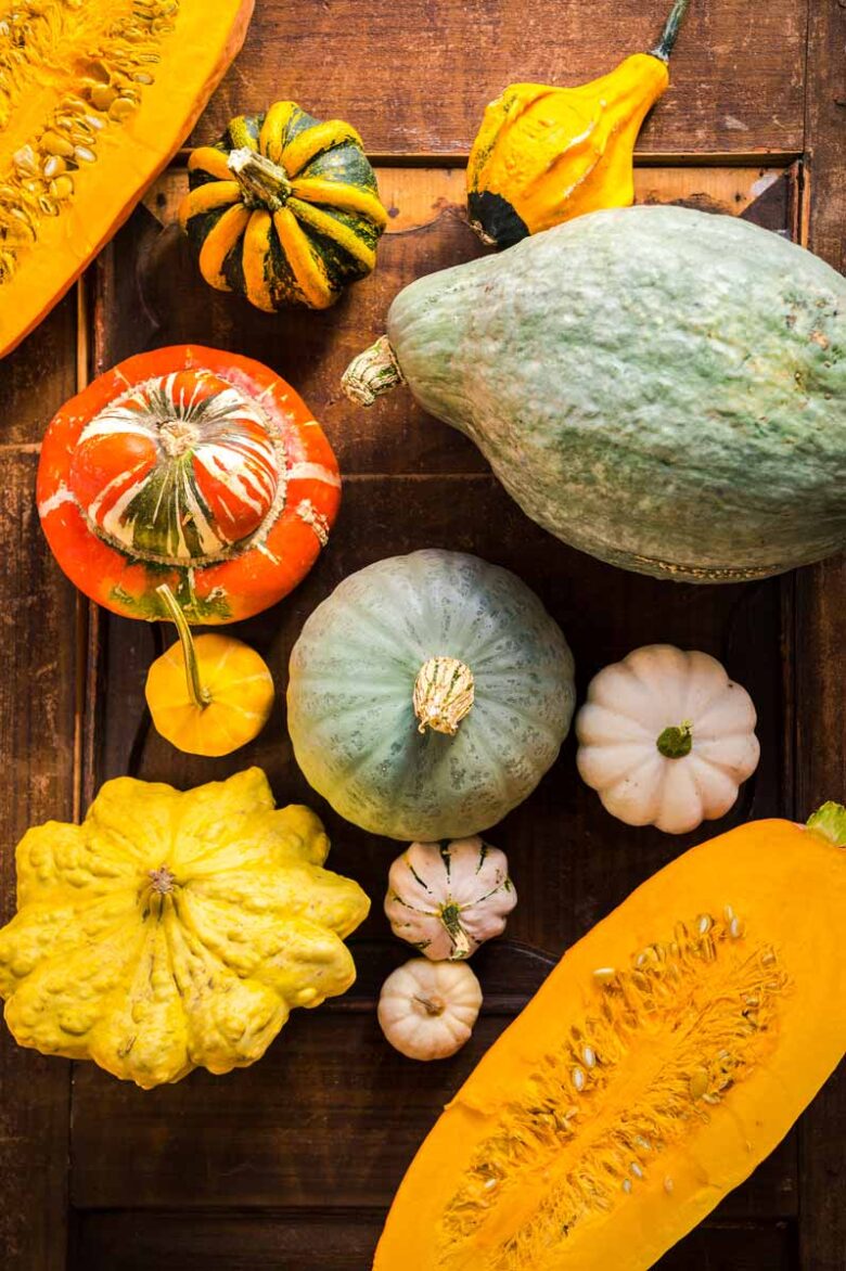 Verschiedene Kürbissorten wie Hokkaido, Butternut und Bischofsmütze liegen auf einem rustikalen Holztisch – perfekte Zutaten für herbstliche Kürbisrezepte.