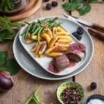 Zart rosa Rehrücken mit fruchtiger Brombeersoße, grünen Bohnen und knusprigen Schupfnudeln auf einem Teller