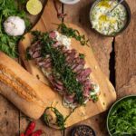 Aufgeschnittenes Steak Sandwich mit saftigem Entrecôte, frittiertem Rucola und Chimichurri Mayonnaise im knusprigen Ciabatta Baguette serviert.