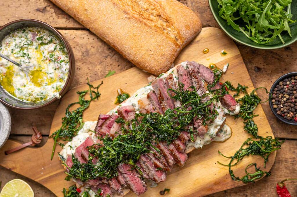 Aufgeschnittenes Steak Sandwich mit saftigem Entrecôte, frittiertem Rucola und Chimichurri Mayonnaise im knusprigen Ciabatta Baguette serviert.