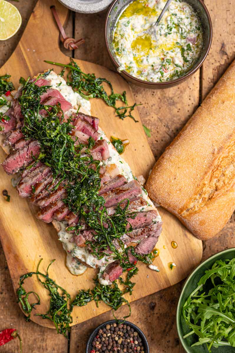 Nahaufnahme vom Steak Sandwich zeigt das rosa gebratene Entrecôte, knusprigen Rucola und cremige Chimichurri Mayonnaise zwischen goldbraunem Ciabatta.
