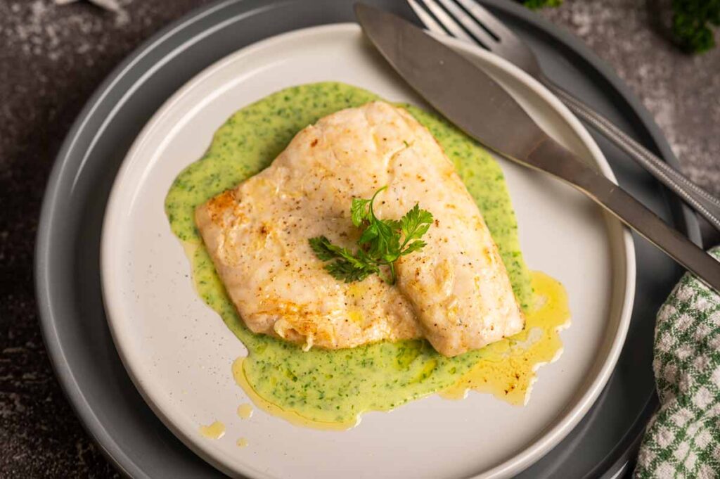 Samtige grüne Kräuter Velouté elegant auf einem Teller mit Wolfsbarschfilet angerichtet