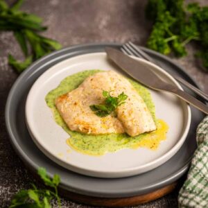 Samtige grüne Kräuter Velouté elegant auf einem Teller mit Wolfsbarschfilet angerichtet