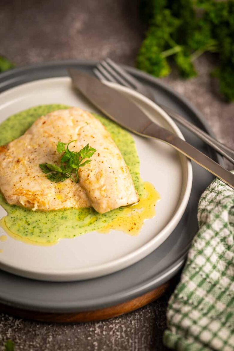 Samtige grüne Kräuter Velouté elegant auf einem Teller mit Wolfsbarschfilet angerichtet