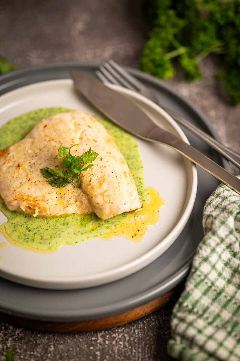 Samtige grüne Kräuter Velouté elegant auf einem Teller mit Wolfsbarschfilet angerichtet