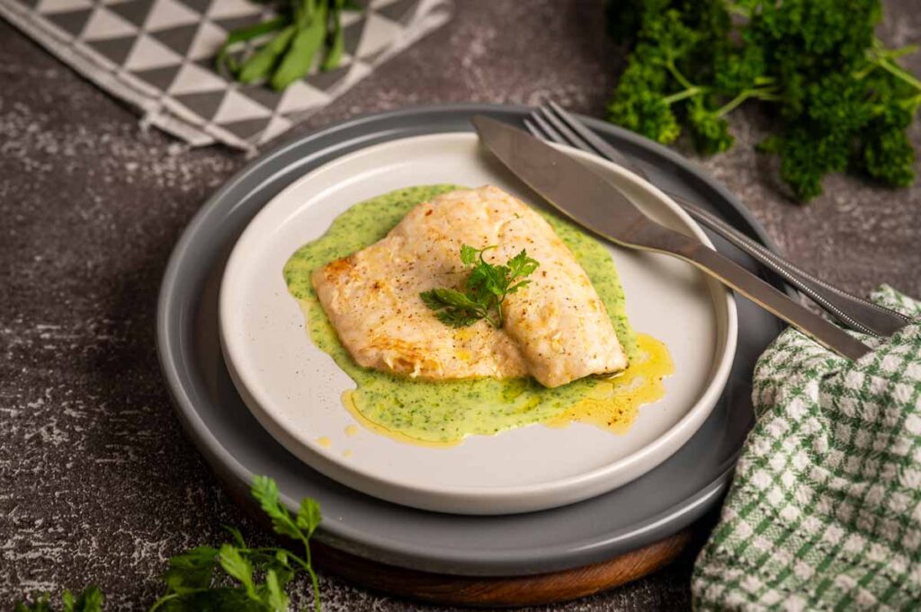 Samtige grüne Kräuter Velouté elegant auf einem Teller mit Wolfsbarschfilet angerichtet