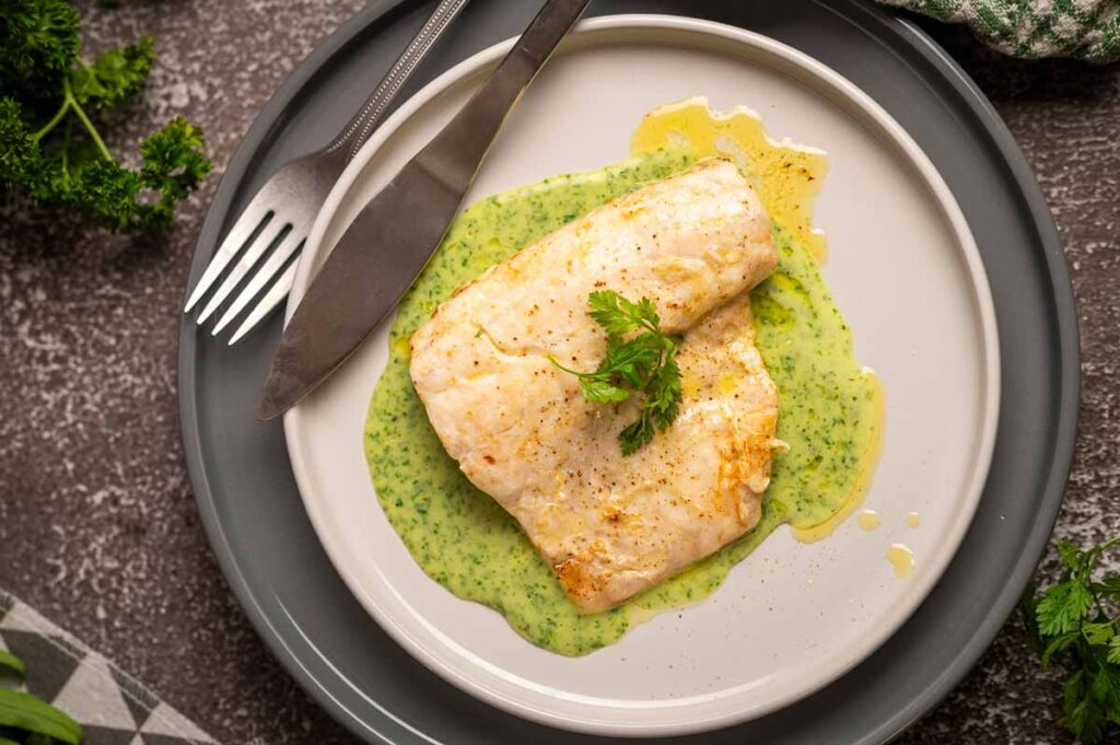 Samtige grüne Kräuter Velouté elegant auf einem Teller mit Wolfsbarschfilet angerichtet