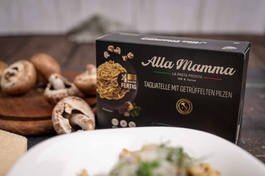 Produktverpackung von alla mamma Pasta neben fertig zubereiteten Tagliatelle mit getrüffelten Pilzen