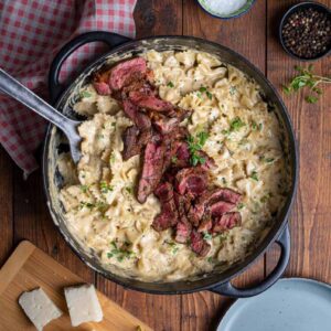 Saftige Steakstreifen auf cremiger Steak Pasta Alfredo mit Parmesan und Farfalle auf einem Teller angerichtet.