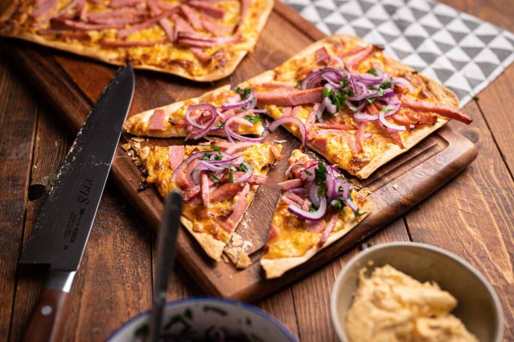 Leberkäs-Flammkuchen mit roten Zwiebeln und Petersilie angerichtet